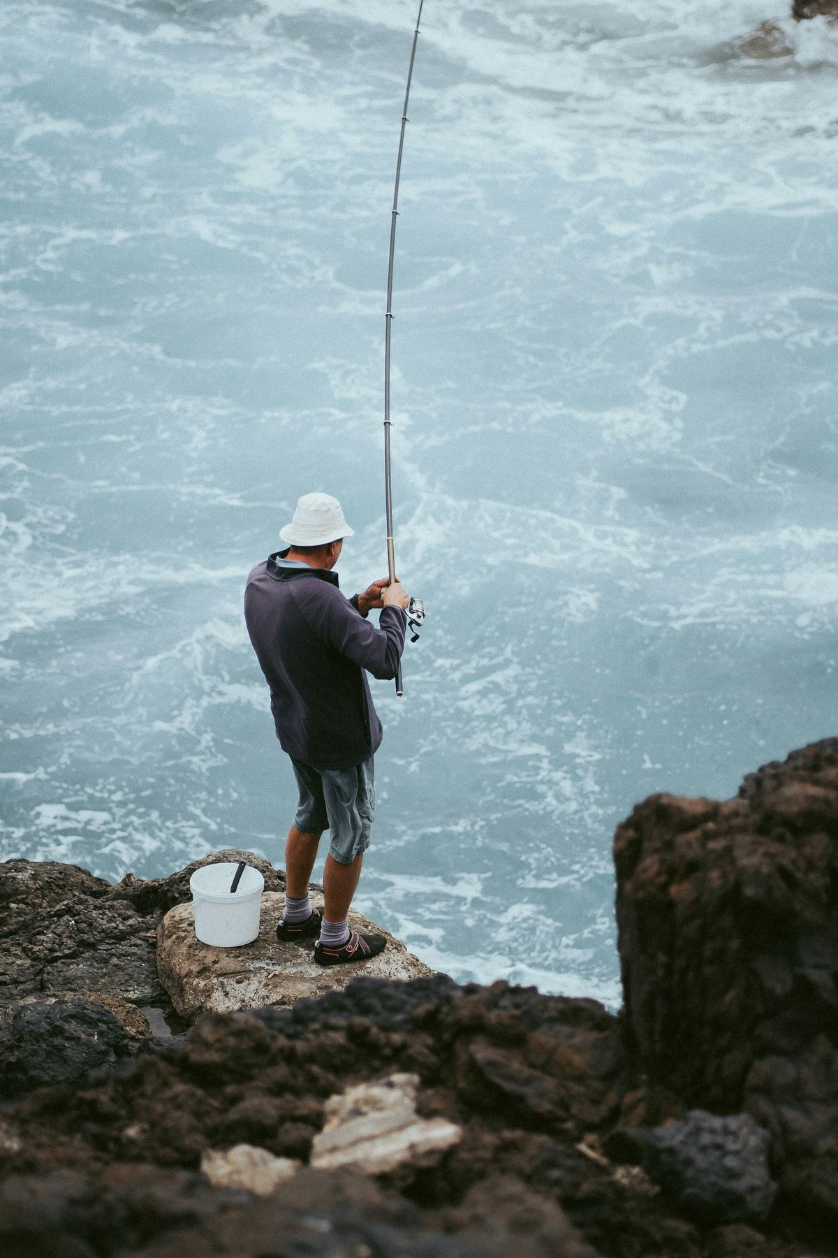 An angler casting from the rocks into heavy surf
